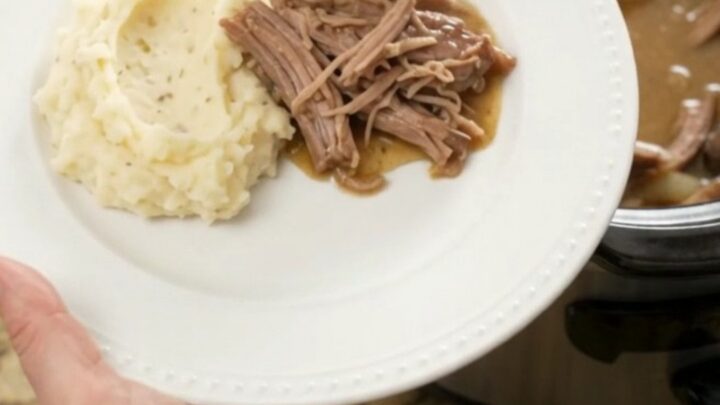 Shredded pork sirloin roast with mushrooms in a slow cooker, topped with butter sauce