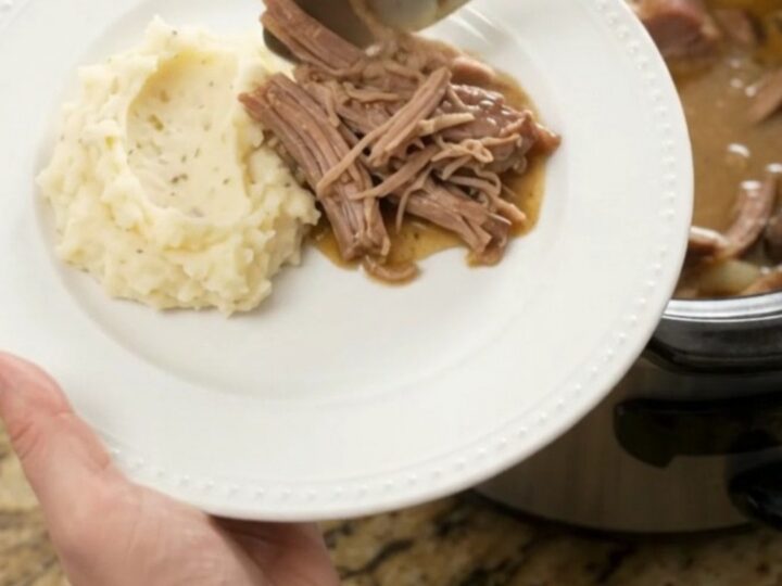 Shredded pork sirloin roast with mushrooms in a slow cooker, topped with butter sauce