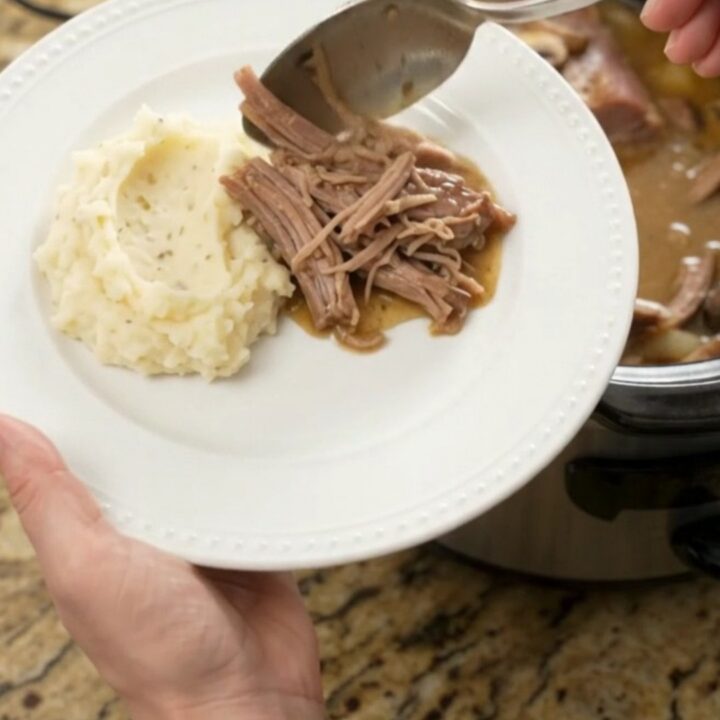 Shredded pork sirloin roast with mushrooms in a slow cooker, topped with butter sauce