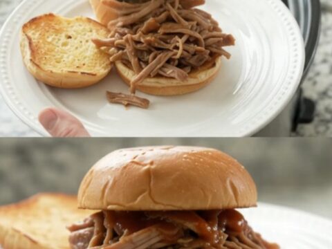 Shredded pork sirloin roast in a glossy brown gravy with whole pepperoncini, in a black slow cooker insert.