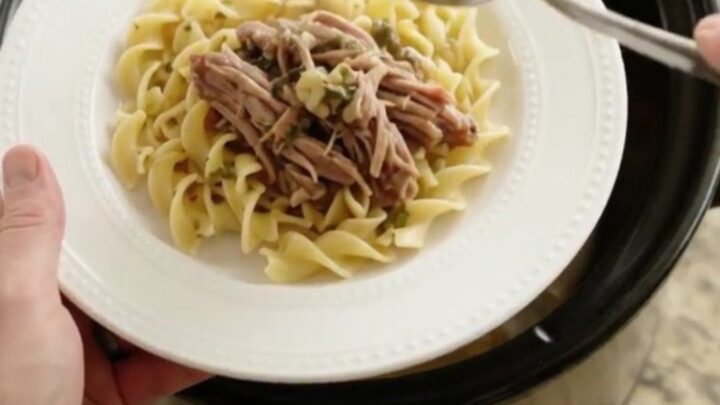 Slow-cooker pork sirloin roast with gravy in a black crockpot, topped with herbs