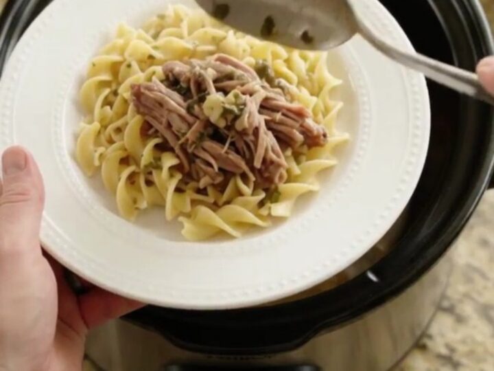 Slow-cooker pork sirloin roast with gravy in a black crockpot, topped with herbs