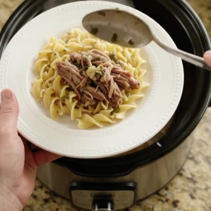 Slow-cooker pork sirloin roast with gravy in a black crockpot, topped with herbs