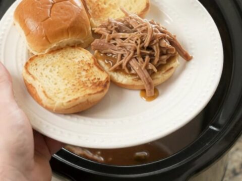 Shredded pork sirloin roast in a slow cooker with rich brown gravy, topped with butter pats