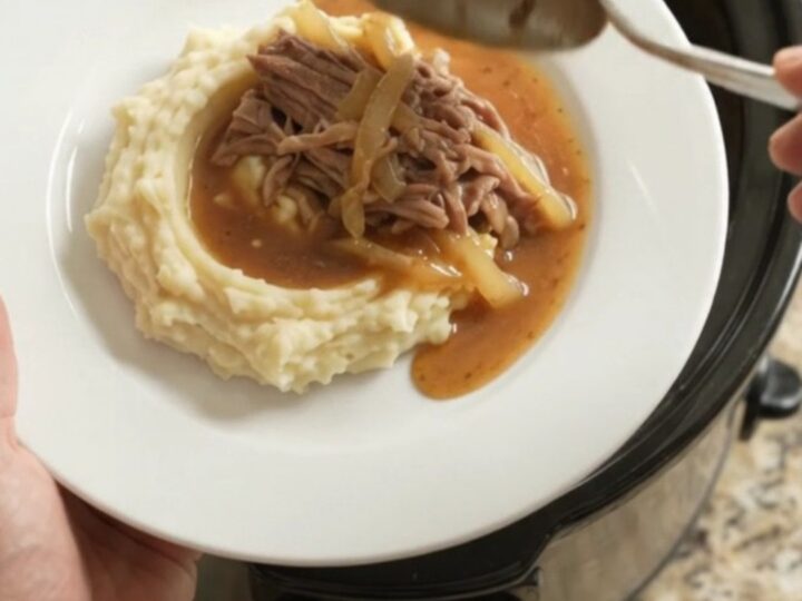 Shredded pork sirloin roast with caramelized onions in a buttery jus in a slow cooker