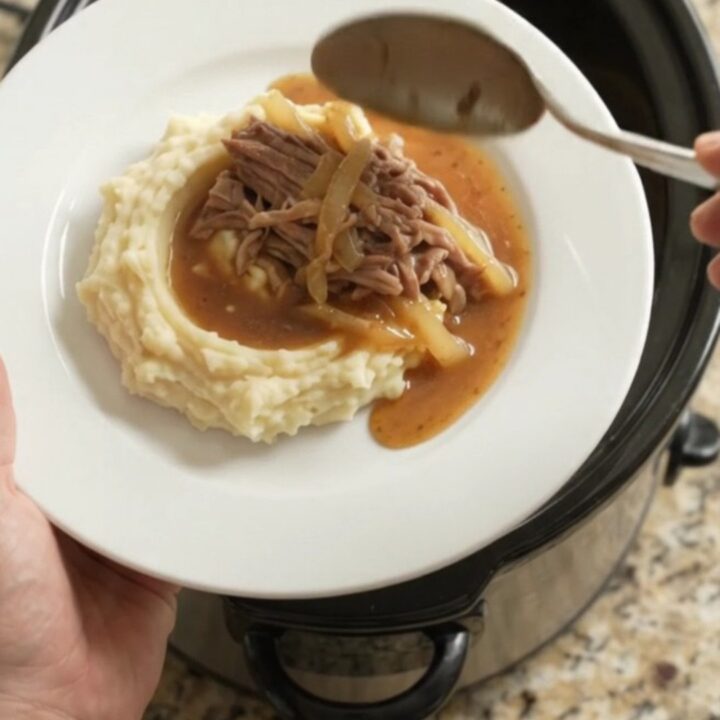 Shredded pork sirloin roast with caramelized onions in a buttery jus in a slow cooker