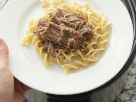 Shredded pork sirloin roast with pearl onions and gravy in a slow cooker, topped with butter medallions.