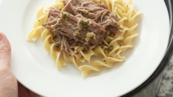 Shredded pork sirloin roast with pearl onions and gravy in a slow cooker, topped with butter medallions.