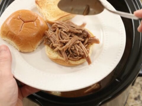 Shredded pork sirloin roast in rich brown gravy with pearl onions in a black slow cooker