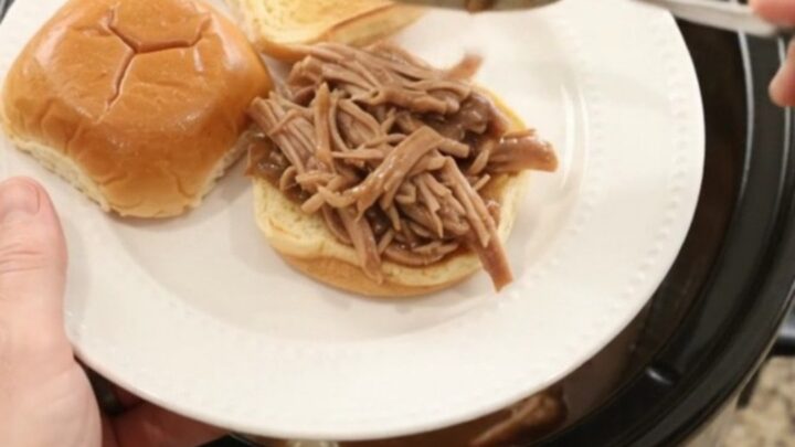 Shredded pork sirloin roast in rich brown gravy with pearl onions in a black slow cooker