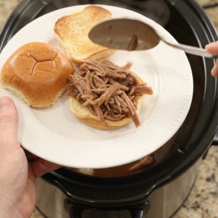 Shredded pork sirloin roast in rich brown gravy with pearl onions in a black slow cooker