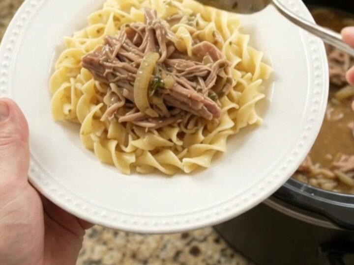 Shredded pork sirloin roast with caramelized onions and garlic butter gravy in a slow cooker