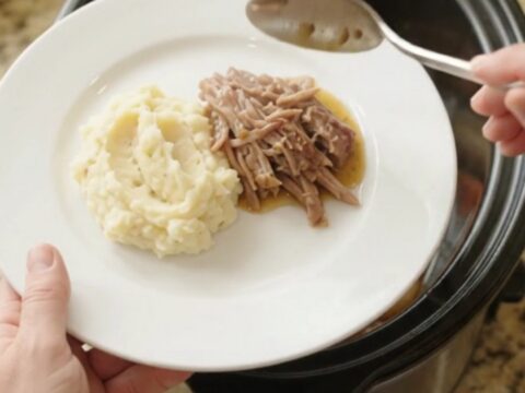 Shredded pork sirloin roast with shallots and carrots in a slow cooker, topped with butter