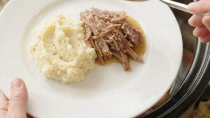 Shredded pork sirloin roast with shallots and carrots in a slow cooker, topped with butter
