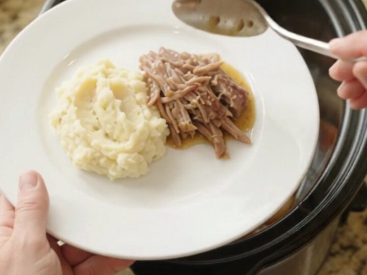 Shredded pork sirloin roast with shallots and carrots in a slow cooker, topped with butter