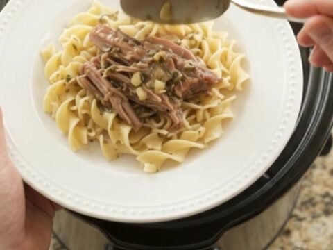 Shredded pork sirloin roast with shallots and carrots in a slow cooker, topped with melted butter and herbs.