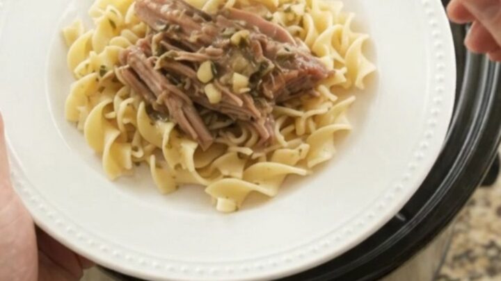 Shredded pork sirloin roast with shallots and carrots in a slow cooker, topped with melted butter and herbs.