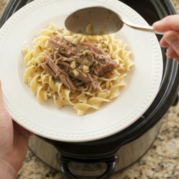 Shredded pork sirloin roast with shallots and carrots in a slow cooker, topped with melted butter and herbs.