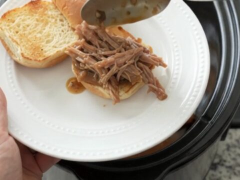 Shredded pork sirloin roast in a slow cooker with rich brown gravy and fresh herbs