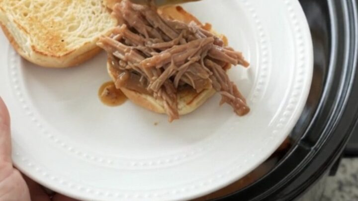 Shredded pork sirloin roast in a slow cooker with rich brown gravy and fresh herbs
