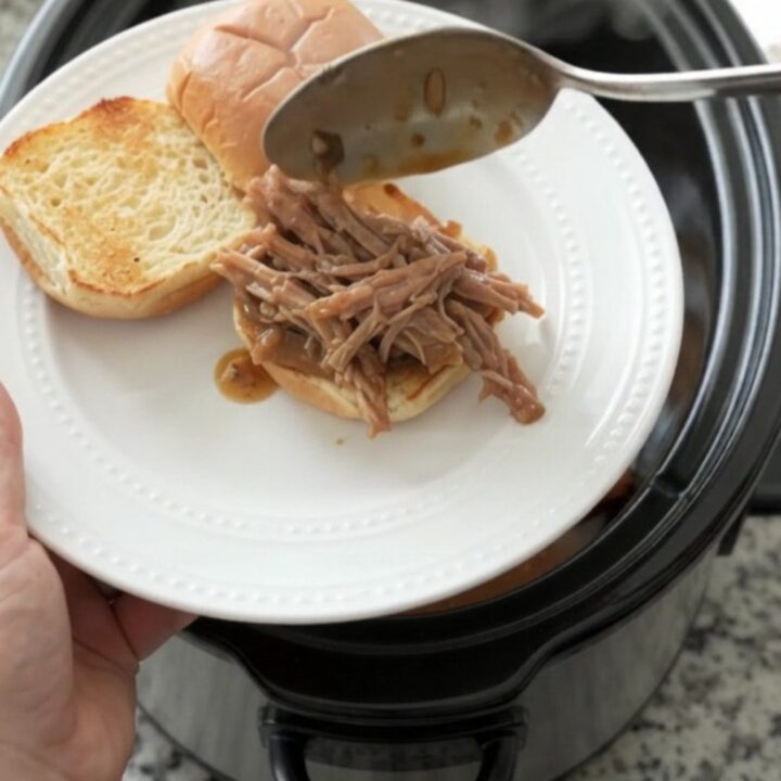 Shredded pork sirloin roast in a slow cooker with rich brown gravy and fresh herbs