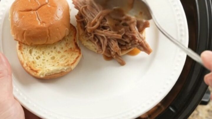 Slow cooker pork sirloin roast with shallots and carrots in rich brown gravy, steaming in the pot.