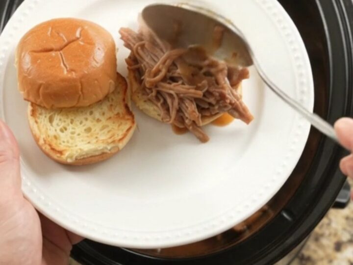 Slow cooker pork sirloin roast with shallots and carrots in rich brown gravy, steaming in the pot.