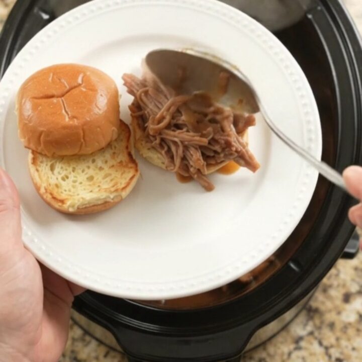 Slow cooker pork sirloin roast with shallots and carrots in rich brown gravy, steaming in the pot.
