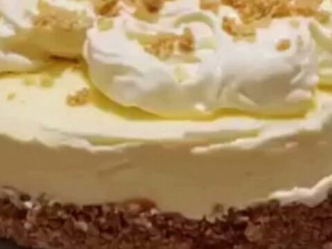 A slice of creamy cheesecake on a white plate with a buttery graham crust and whipped cream.