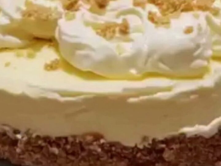 A slice of creamy cheesecake on a white plate with a buttery graham crust and whipped cream.