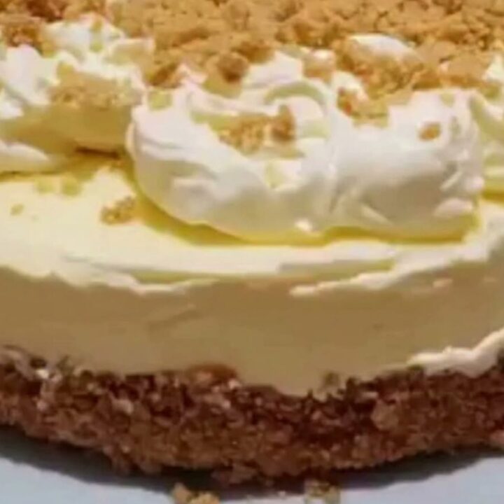 A slice of creamy cheesecake on a white plate with a buttery graham crust and whipped cream.
