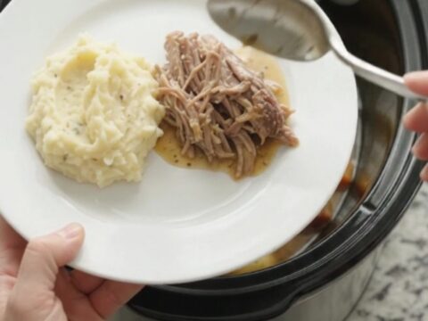 Slow cooker pork sirloin roast with butter and vegetables in a black crockpot.