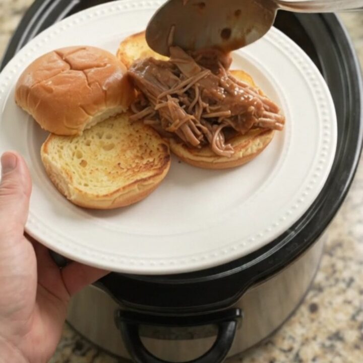 Slow-cooker pork sirloin roast with potatoes and carrots in rich brown gravy, garnished with fresh herbs.