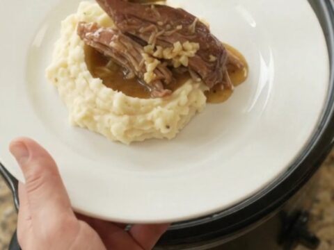Shredded pork sirloin roast with portobello mushrooms in a slow cooker, glistening with butter sauce