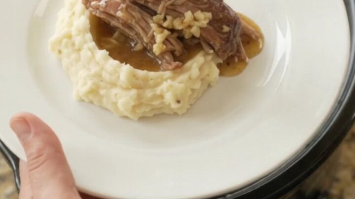 Shredded pork sirloin roast with portobello mushrooms in a slow cooker, glistening with butter sauce