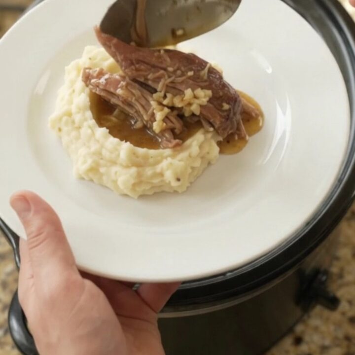 Shredded pork sirloin roast with portobello mushrooms in a slow cooker, glistening with butter sauce