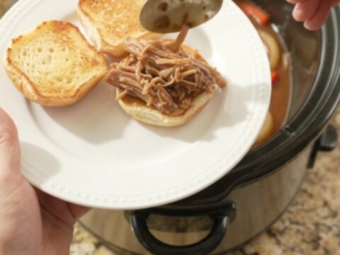 Shredded pork sirloin with sweet peppers and gravy in a slow cooker, garnished with fresh parsley.