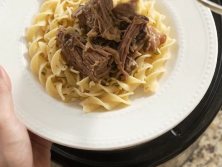Slow-cooker beef roast with mushrooms and garlic butter gravy in a black ceramic crockpot