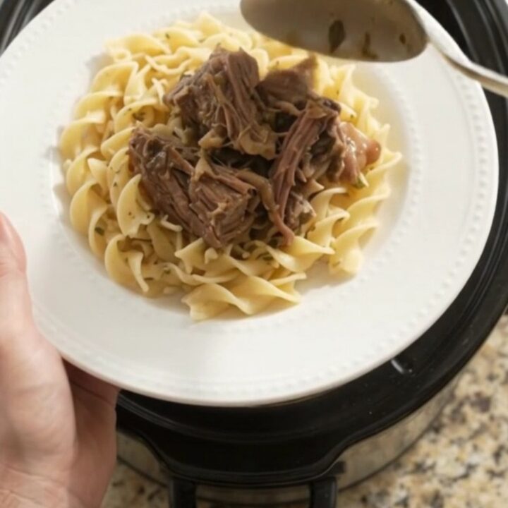 Slow-cooker beef roast with mushrooms and garlic butter gravy in a black ceramic crockpot