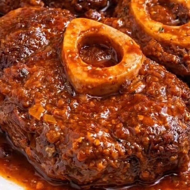 A close-up of a tender braised veal shank with rich sauce and crispy roasted potatoes on a plate.