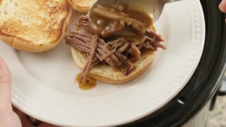 Shredded slow-cooked beef roast in rich brown gravy in a black Crockpot