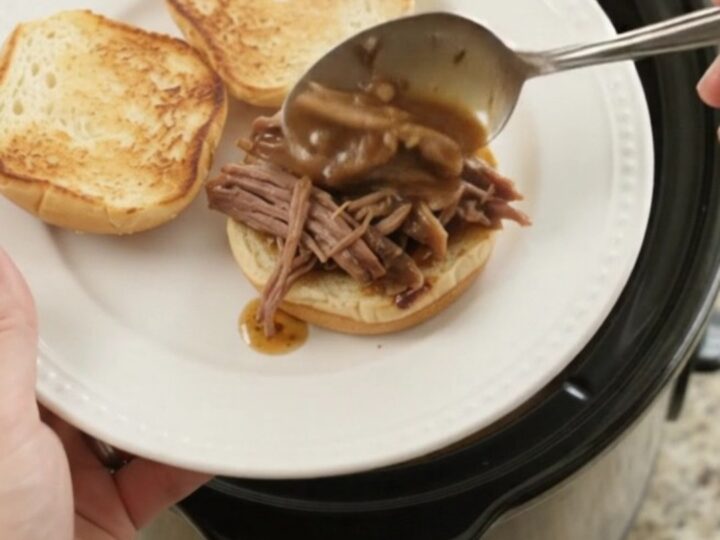 Shredded slow-cooked beef roast in rich brown gravy in a black Crockpot