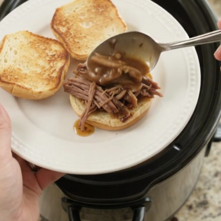Shredded slow-cooked beef roast in rich brown gravy in a black Crockpot