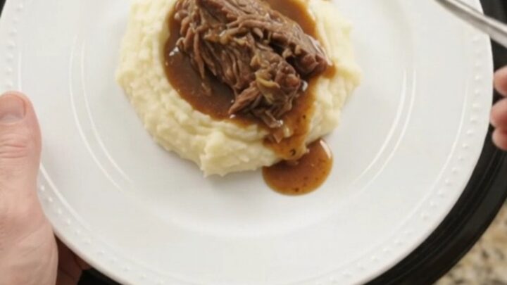 Slow cooker Guinness onion butter roast in a black crockpot, with pearl onions and rich jus.
