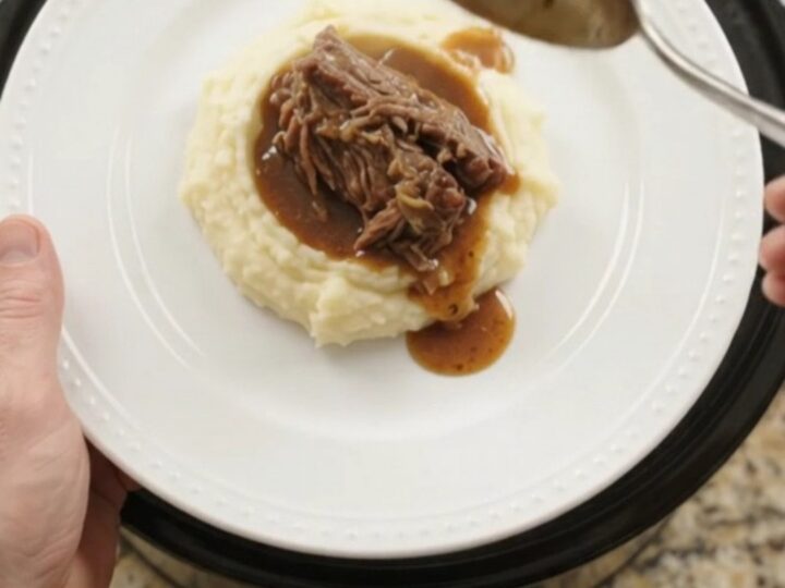 Slow cooker Guinness onion butter roast in a black crockpot, with pearl onions and rich jus.