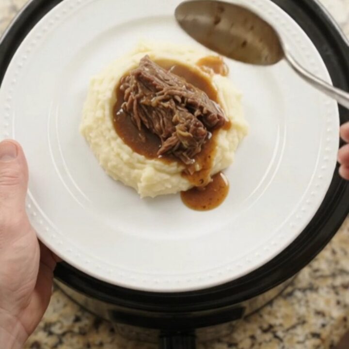 Slow cooker Guinness onion butter roast in a black crockpot, with pearl onions and rich jus.