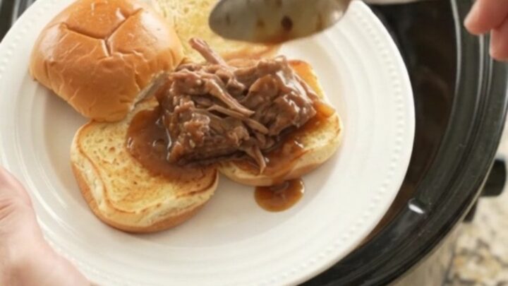 Shredded beef and onions in a dark gravy in a slow cooker