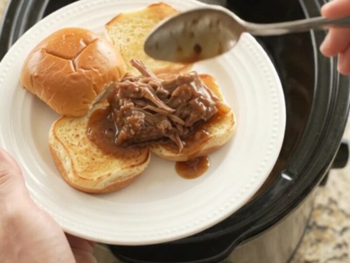 Shredded beef and onions in a dark gravy in a slow cooker