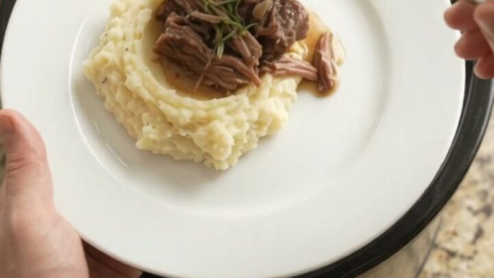 A fork-tender bottom round roast in a slow cooker with garlic and herbs, golden jus bubbling around it.