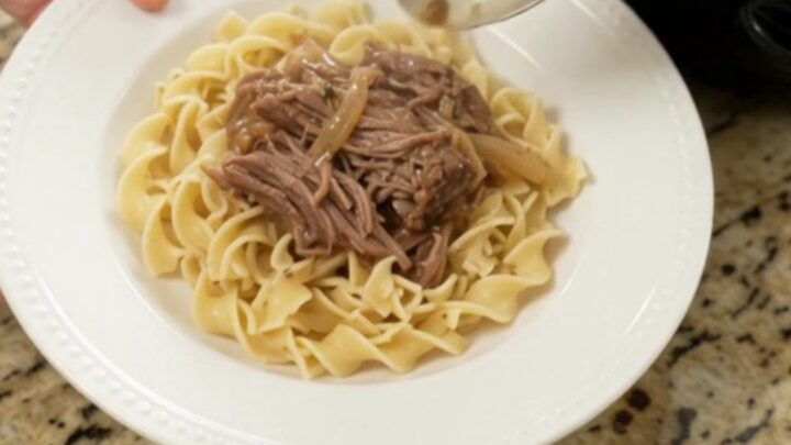 Slow cooker French onion garlic butter roast with caramelized onions and gravy, served on a white plate